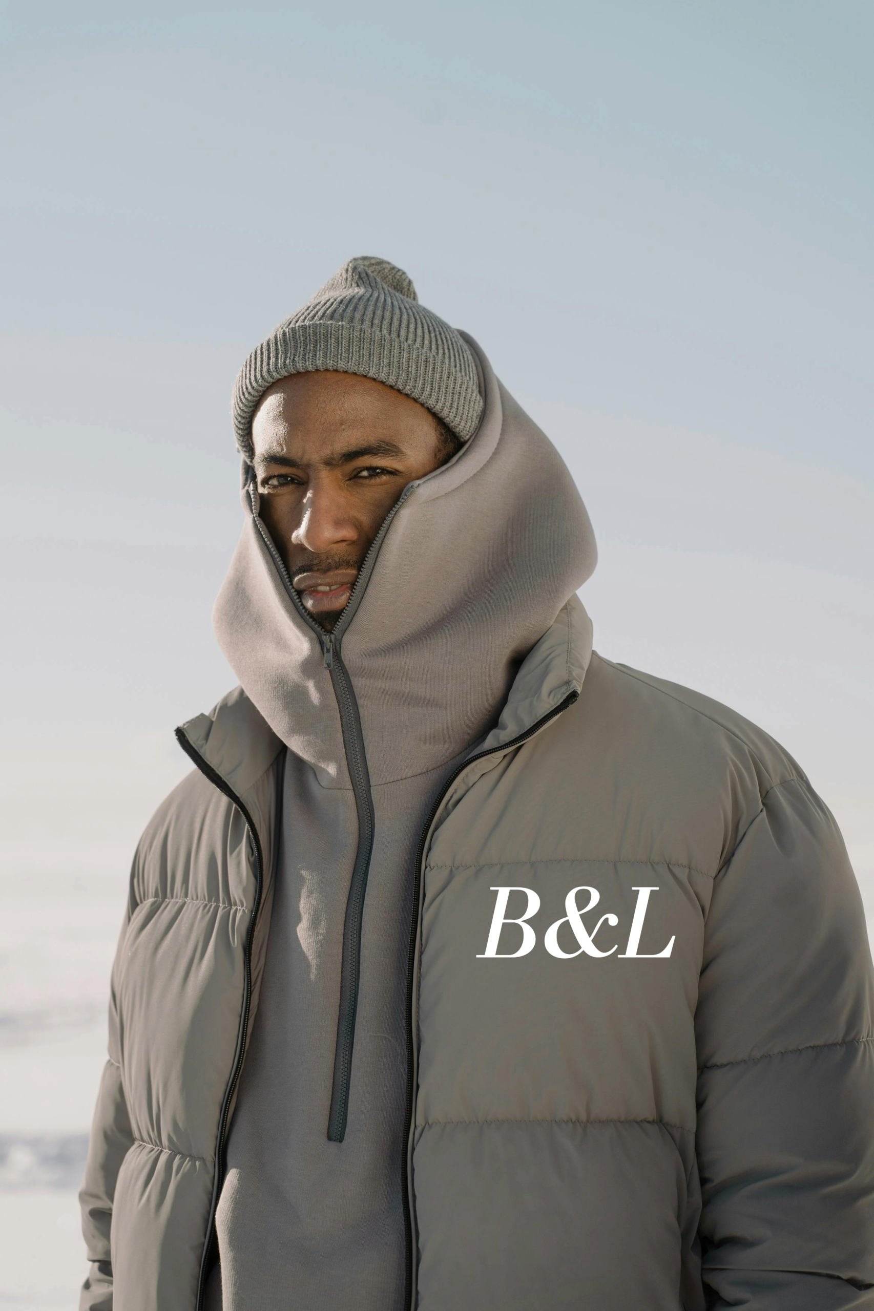 manteau horizon Mannequin portant la doudoune matelassée grise B&L avec sweat à capuche assorti et bonnet gris dans un paysage de neige - Streetwear Hiver."
